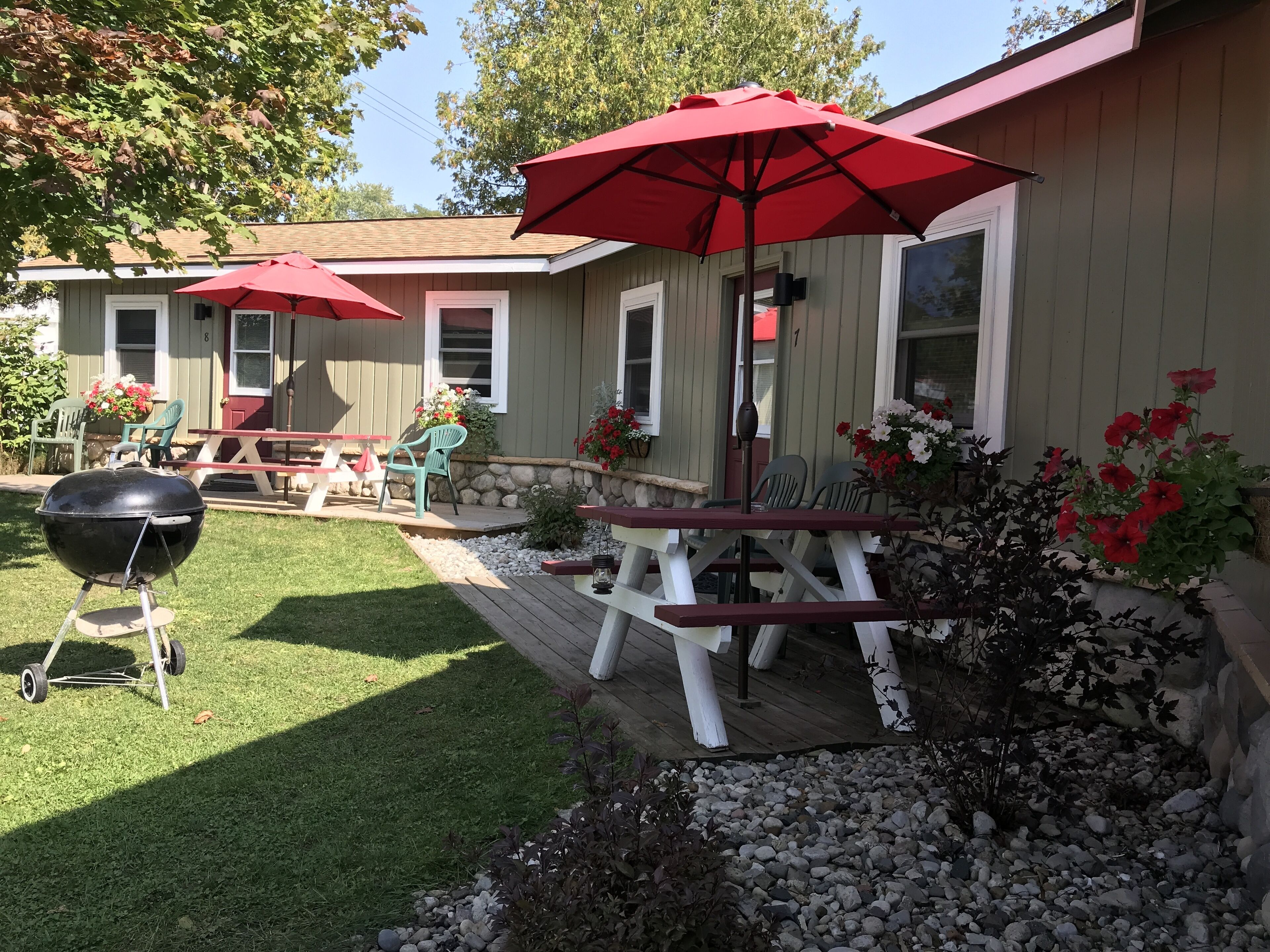 A patio with a barbecue grill, outdoor seating, and red umbrellas.