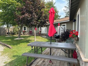 A patio with a table and benches, a grill, and a tree.