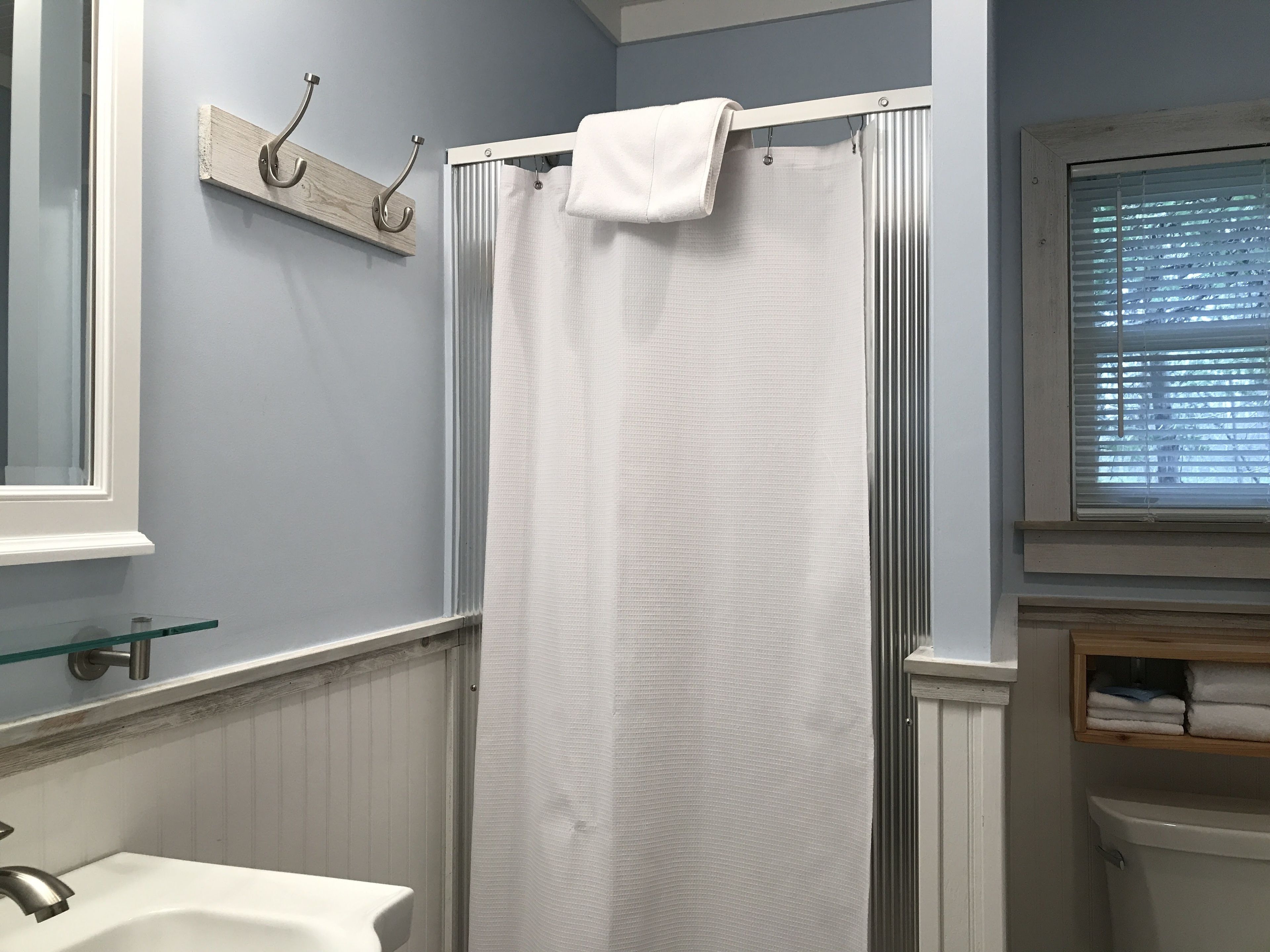 Une salle de bain avec un rideau de douche, un lavabo et une fenêtre avec des stores.