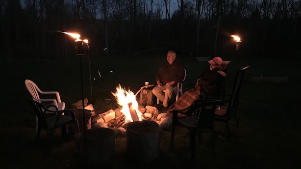 A group of people sitting around a campfire in a dark outdoor setting with trees in the background. - Cedar Ridge Cabins (Honor)