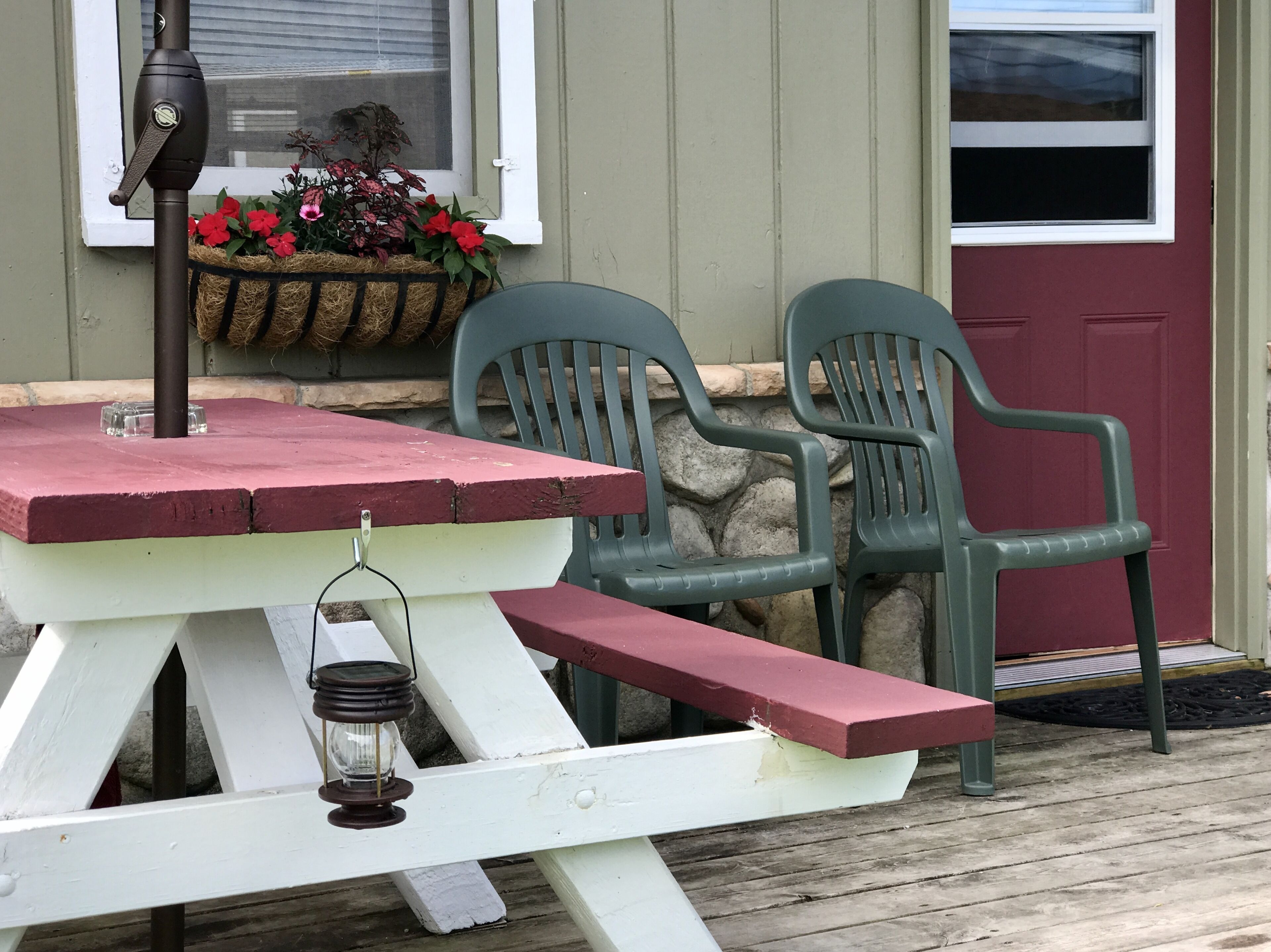 Une table de pique-nique avec une lanterne et un pot de fleurs placés près d’une fenêtre.