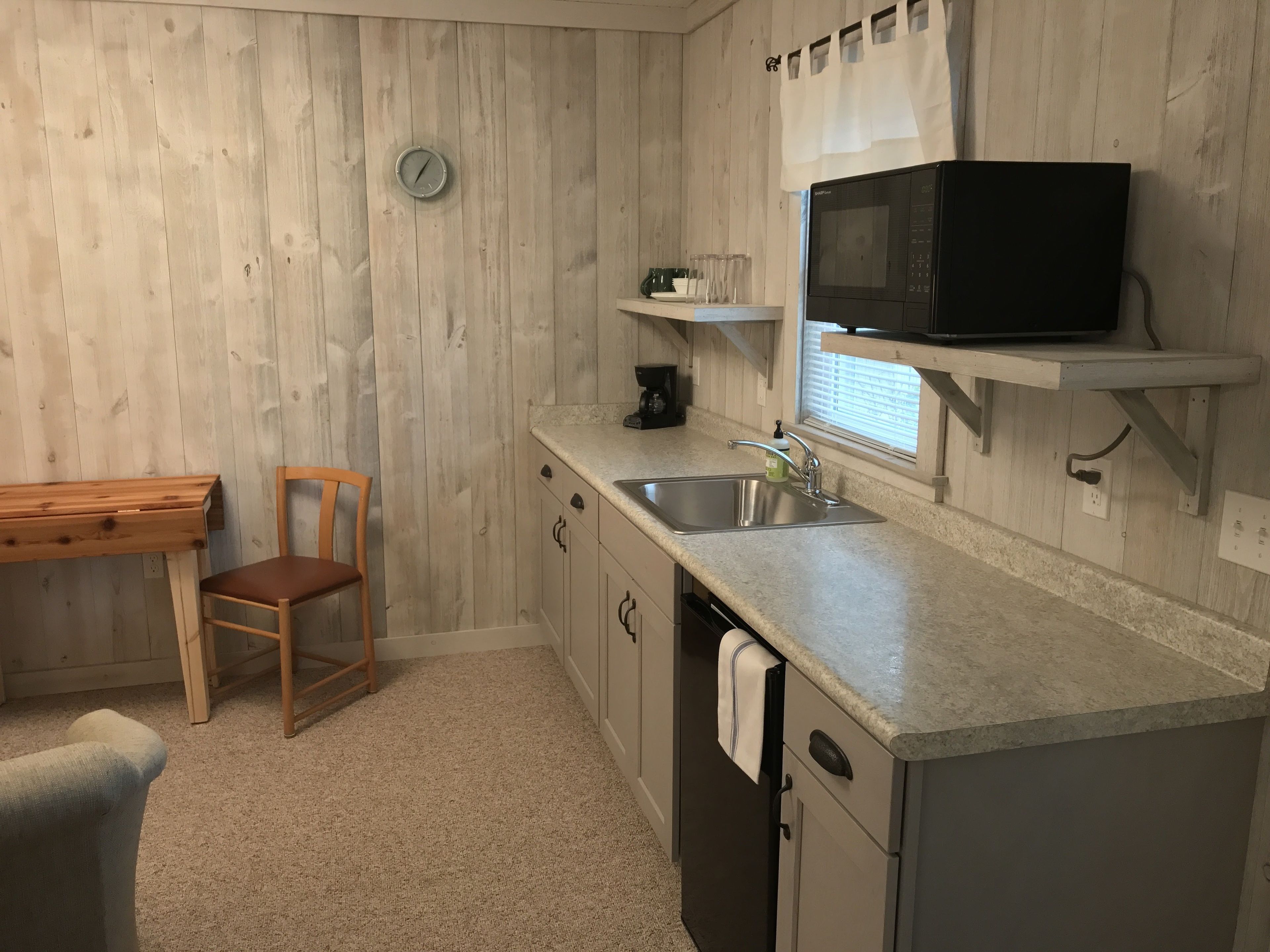 A compact kitchen with a wooden wall, a microwave, a sink, and a small window.