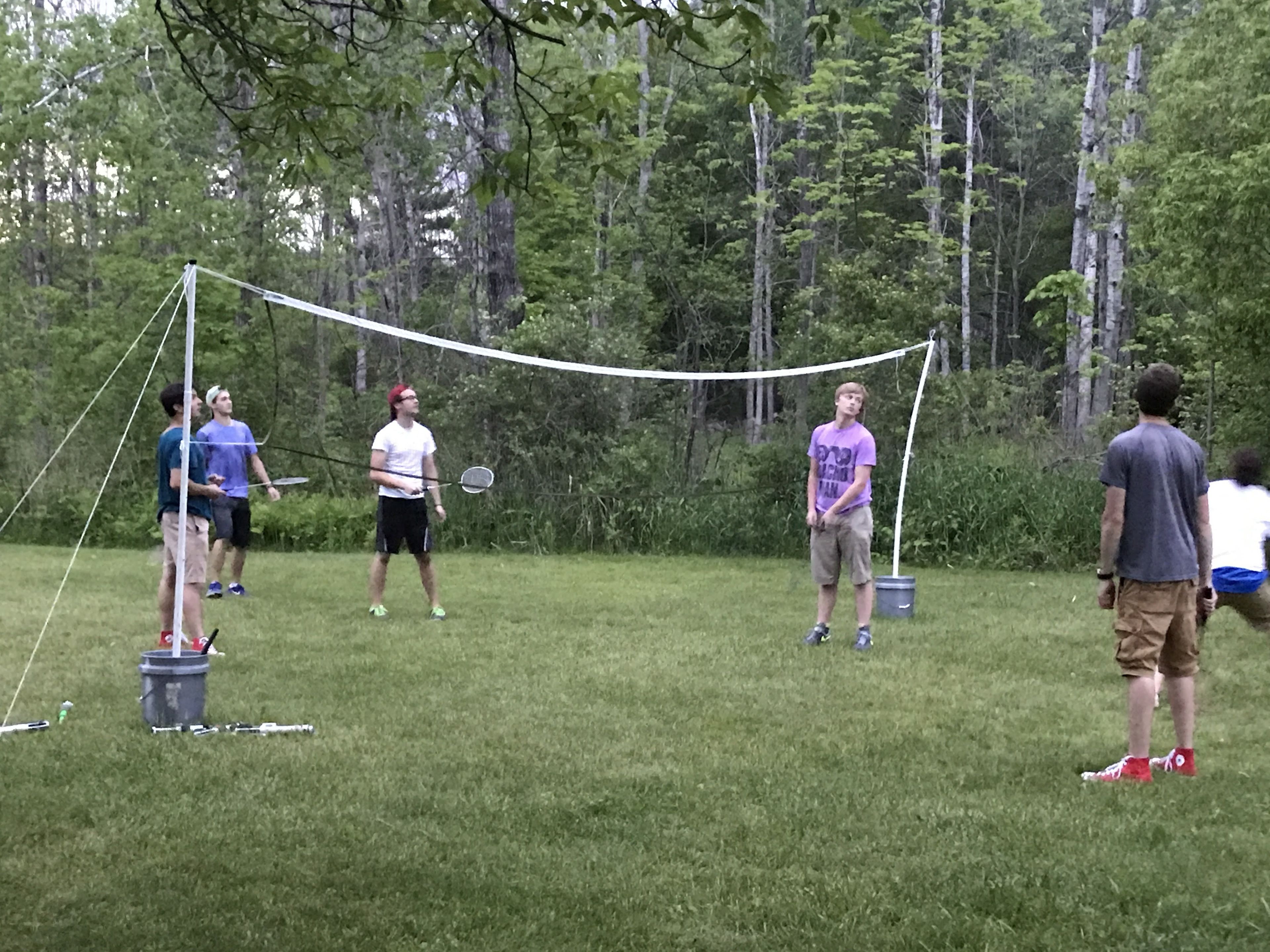 Un grupo de personas jugando bádminton al aire libre, con una red y volante en el suelo.