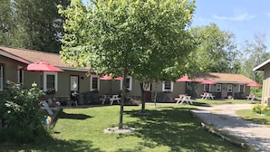 A residential area with a house, a barbecue grill, and outdoor seating with red umbrellas. - Cedar Ridge Cabins (Honor)