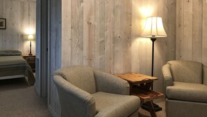 A room with a bed, two armchairs, a wooden table, and a floor lamp. - Cedar Ridge Cabins (Honor)