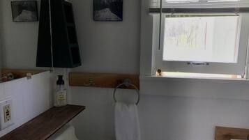Un baño con un lavamanos blanco, una estantería de madera, un perchero para toallas y una ventana con persianas.