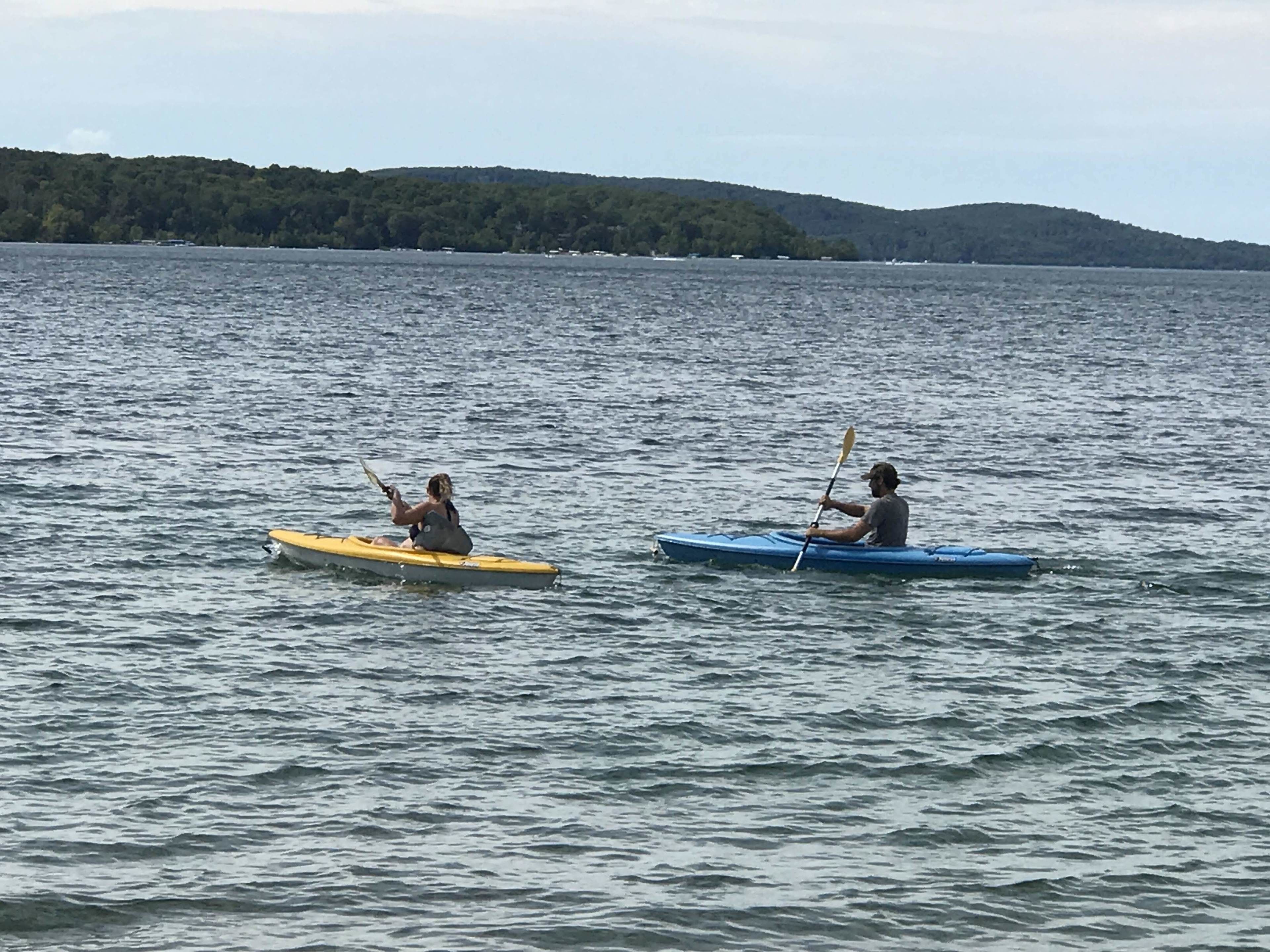 Zwei Kajaks auf dem Wasser, im Hintergrund ein bewaldeter Hügel.
