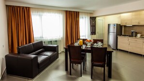 A modern living room with a sofa, dining table, chairs, and a kitchen area with cabinets and appliances. - Crystal Hill Villas (Borjomi)