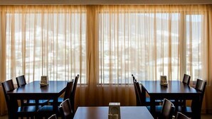 A conference room with two tables and chairs, large windows with sheer curtains, and a radiator on the wall. - Crystal Hill Villas (Borjomi)