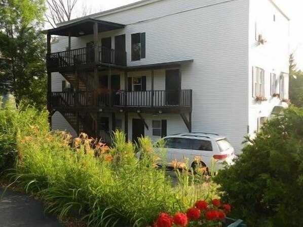 A multi-story building with balconies and a car parked in front.
