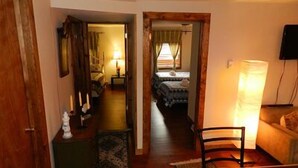 A narrow hallway leading to a bedroom with a bed, a nightstand, and a lamp. There is a wooden door on the left and a chair in the foreground. - Blue Frost Apartments (Lake Placid)