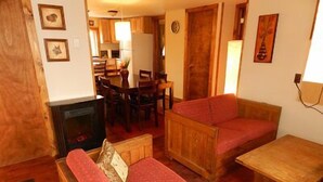 A cozy living room with a fireplace, wooden furniture, and a dining area in the background. - Blue Frost Apartments (Lake Placid)