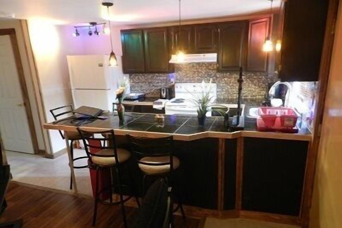 A compact kitchen with a central island, bar stools, and a refrigerator.