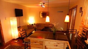 A cozy living room with a sofa, a coffee table, and a dining table. There are two pendant lights hanging above the table. - Blue Frost Apartments (Lake Placid)