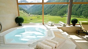 Un cuarto de spa con hidromasaje, ventanas amplias y vistas a montañas.