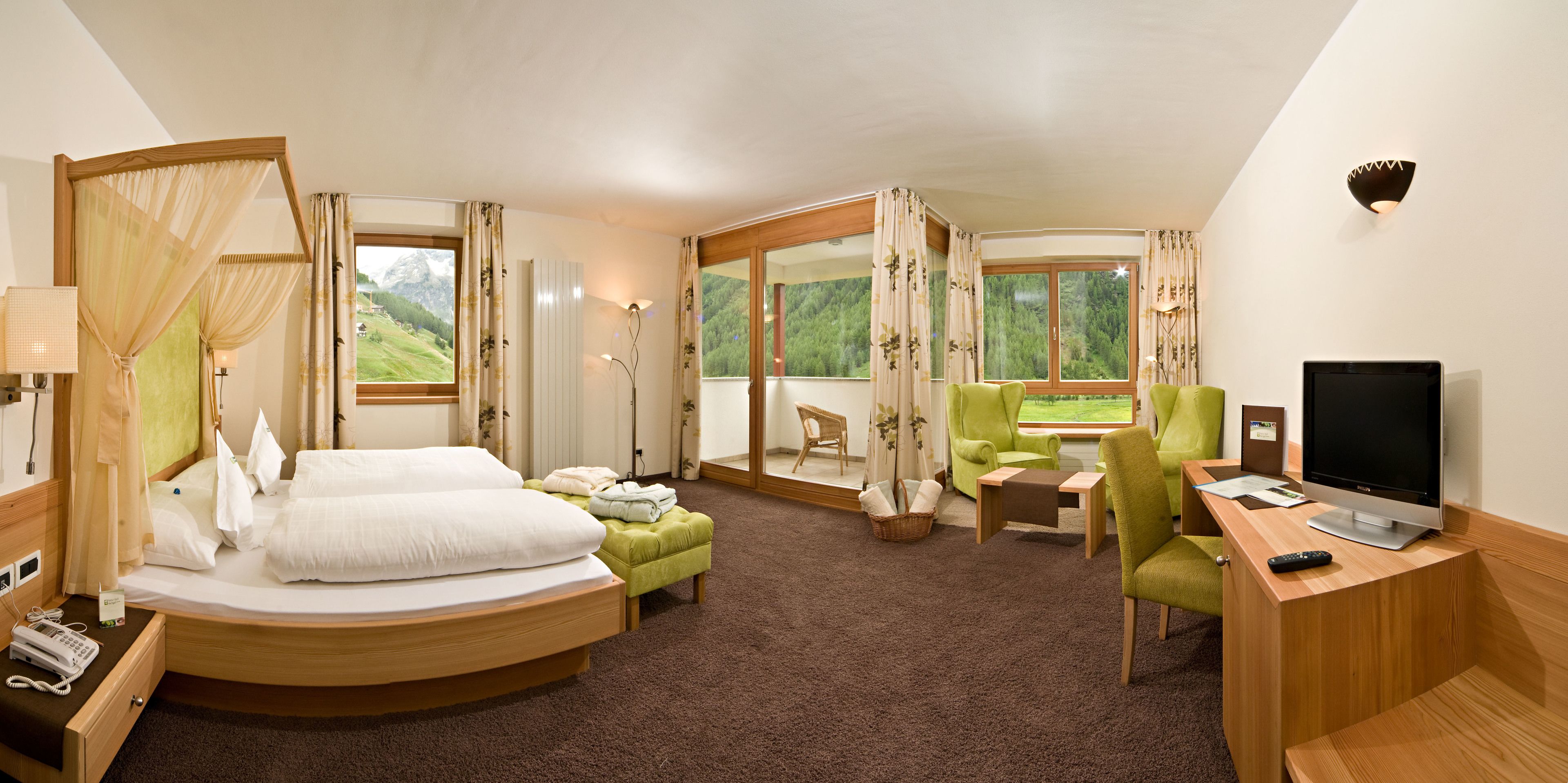 Ein Hotelzimmer mit Bett, Schreibtisch mit Fernseher, Stuhl und Blick ins Freie.
