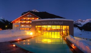 Un hôtel avec une piscine à l’avant, entouré de neige et de montagnes.