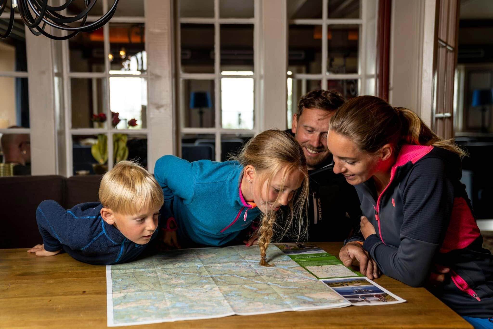 A family of four around a table with a map, in a room with large windows and a chandelier.