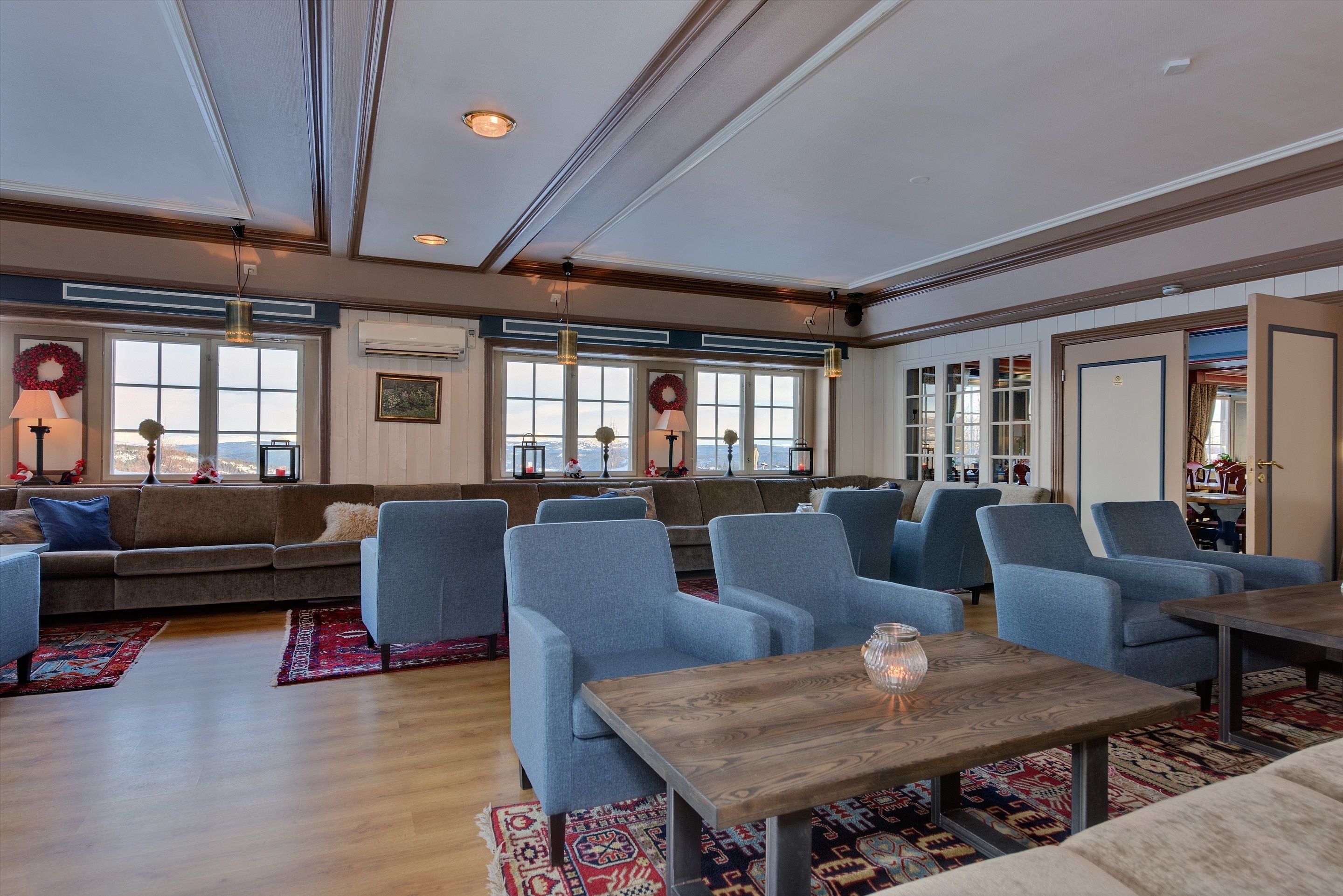 A spacious lounge area with a sofa, multiple armchairs, a wooden table, and a view through large windows.