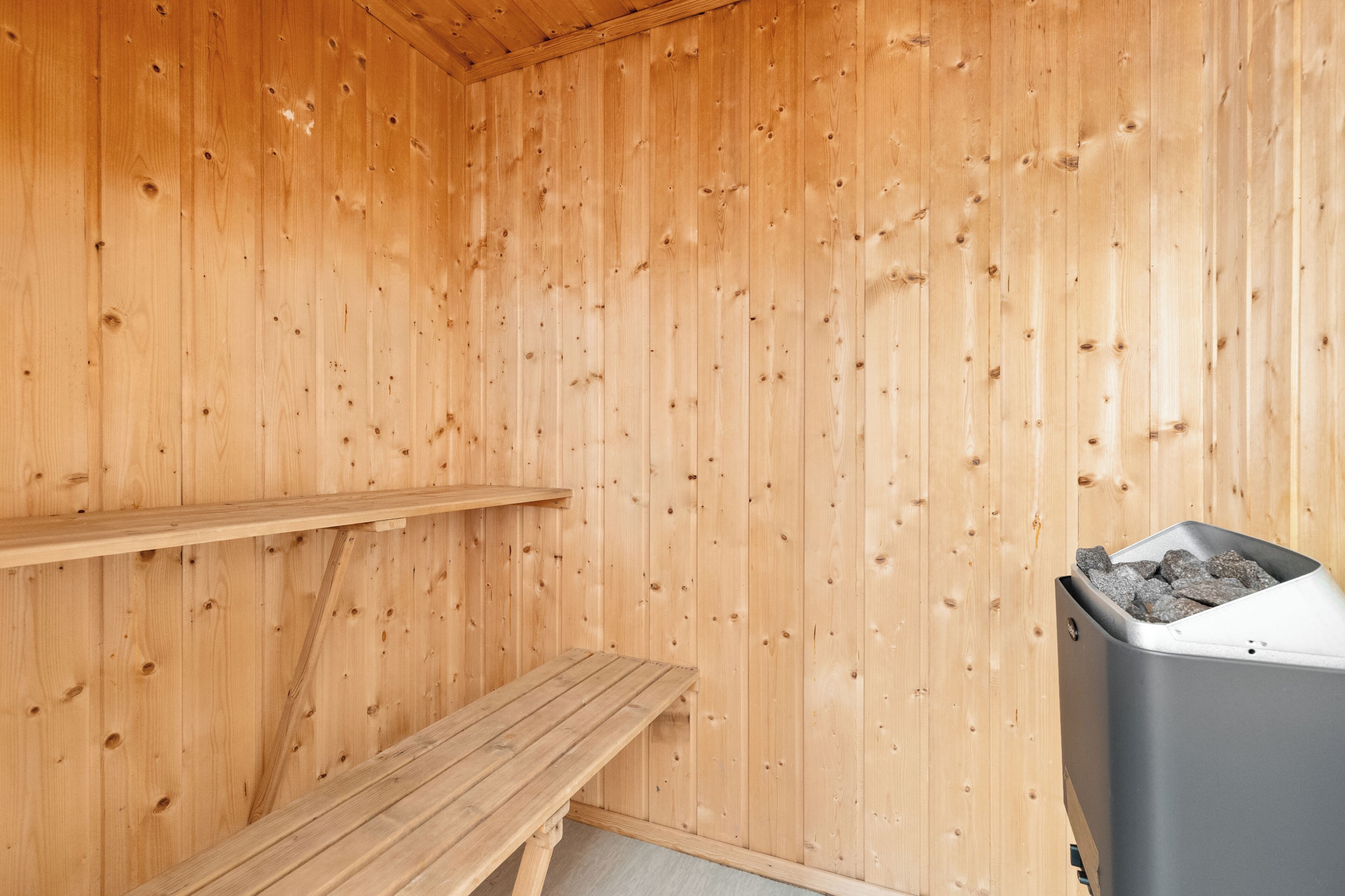 Een houten sauna met een bank en een prullenbak.