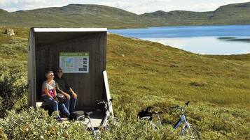 A wooden shelter with a map and information board, two people sitting inside, and bicycles outside.