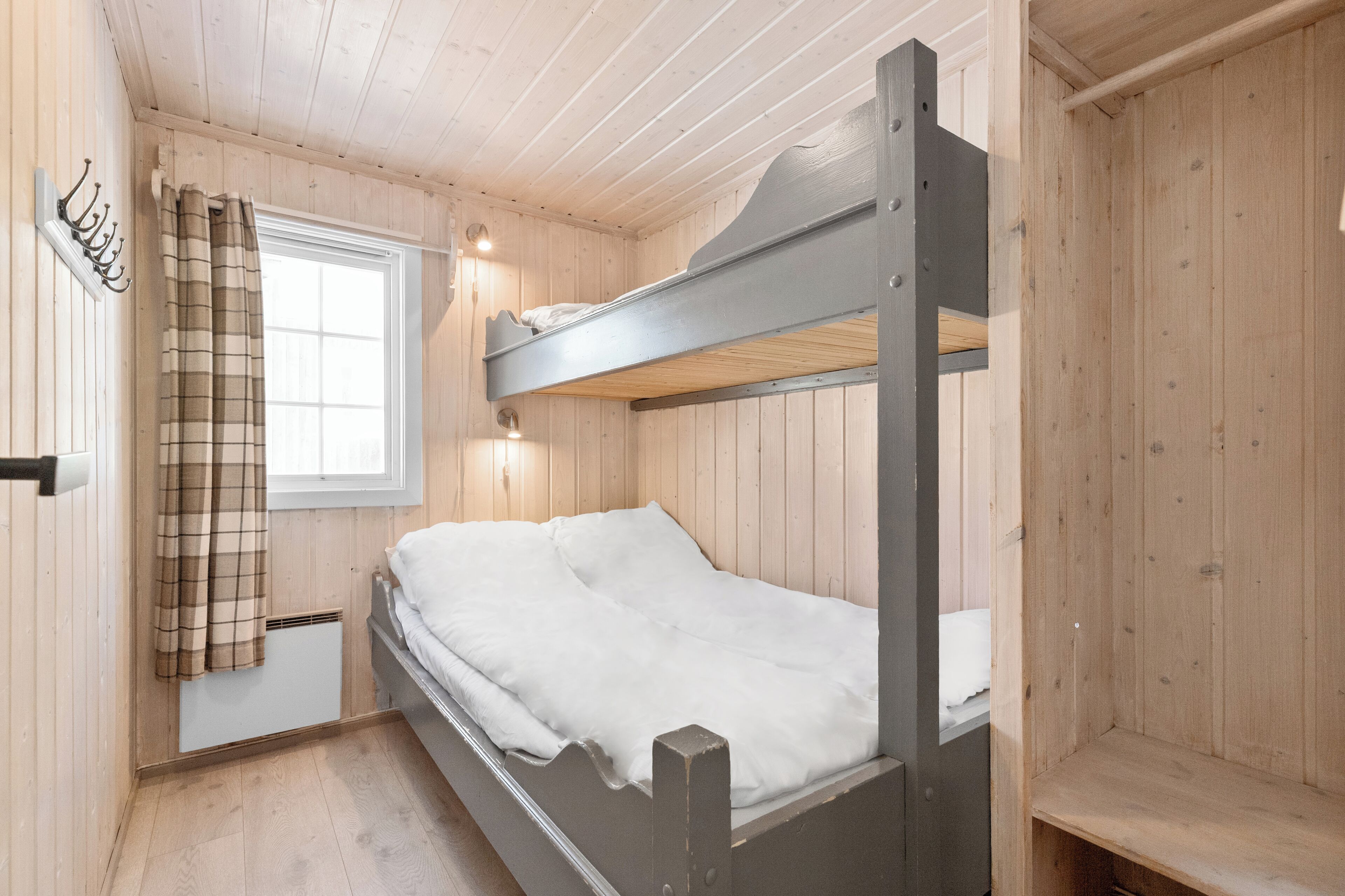 A bunk bed in a wooden room with a window, a heater, and a coat rack.