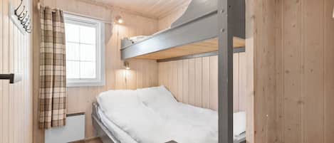 A bunk bed in a wooden room with a window, a heater, and a coat rack.