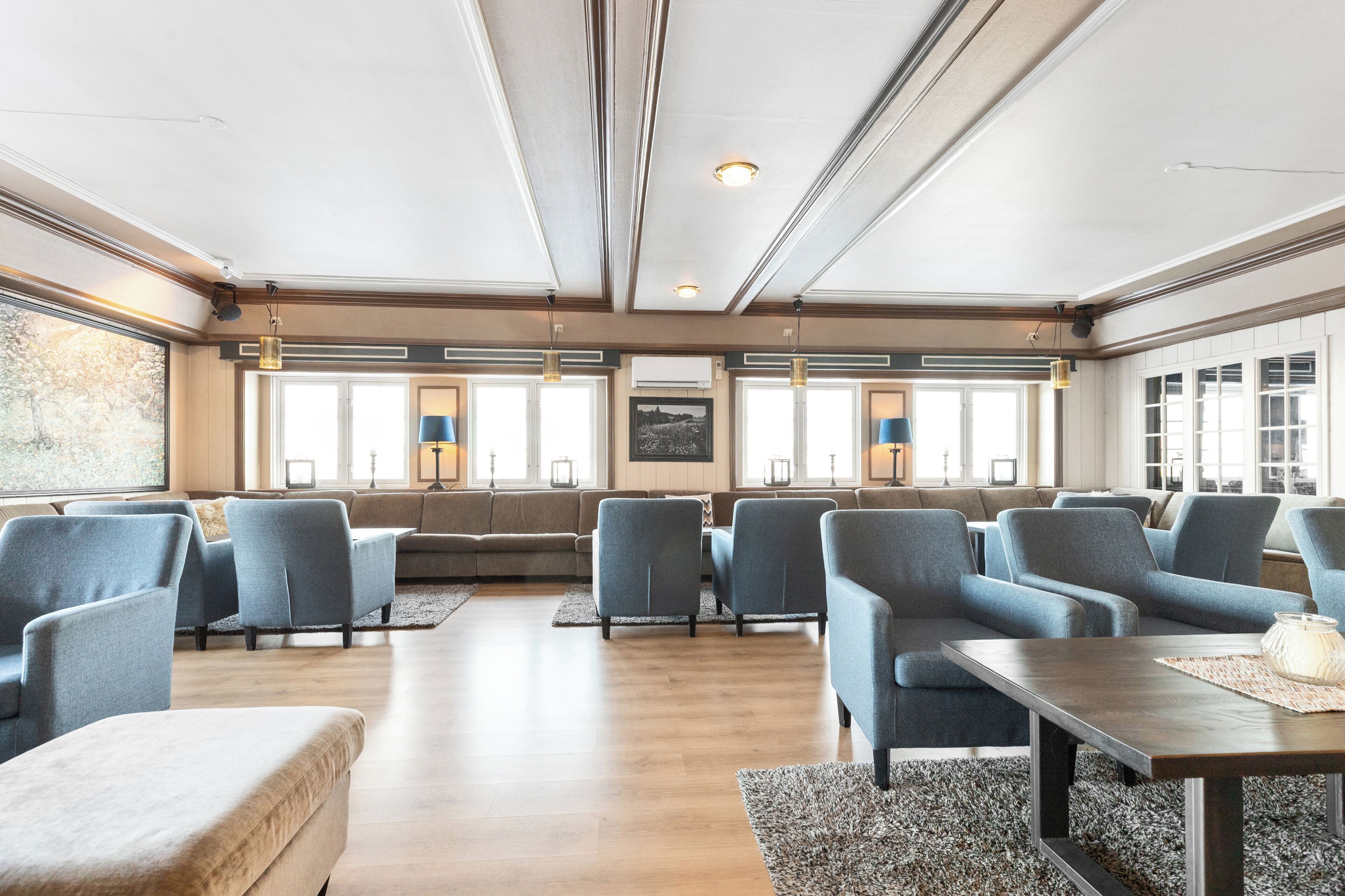 A spacious lounge with multiple seating areas, large windows, and a central table.