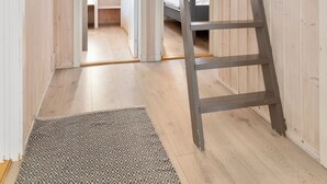 A wooden interior with a ladder, a patterned rug, and a door leading to another room. - Gomobu Fjellstue (Vestre Slidre)