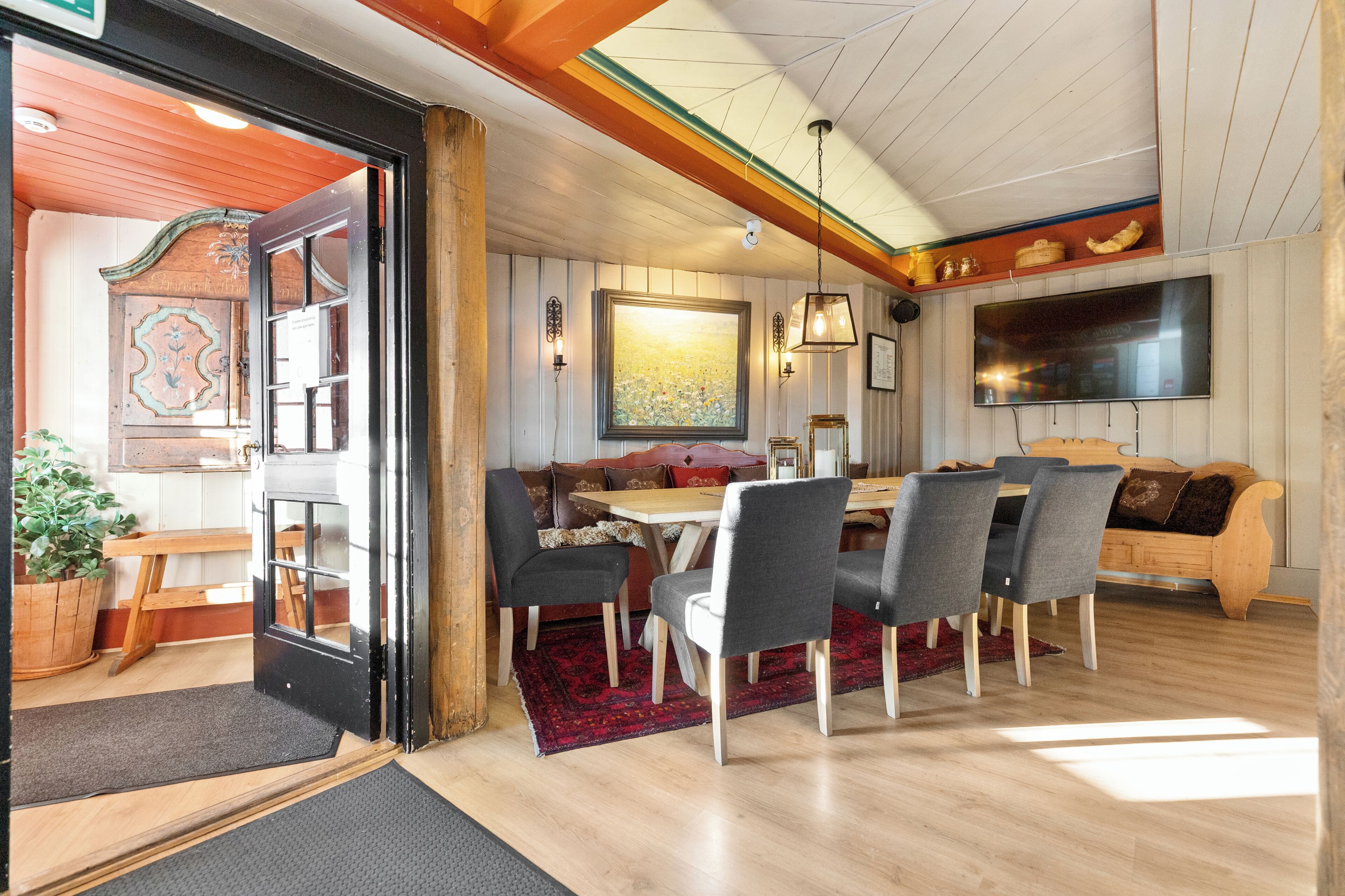 A dining area with a table and chairs, a sofa, a television, and a wooden ceiling.