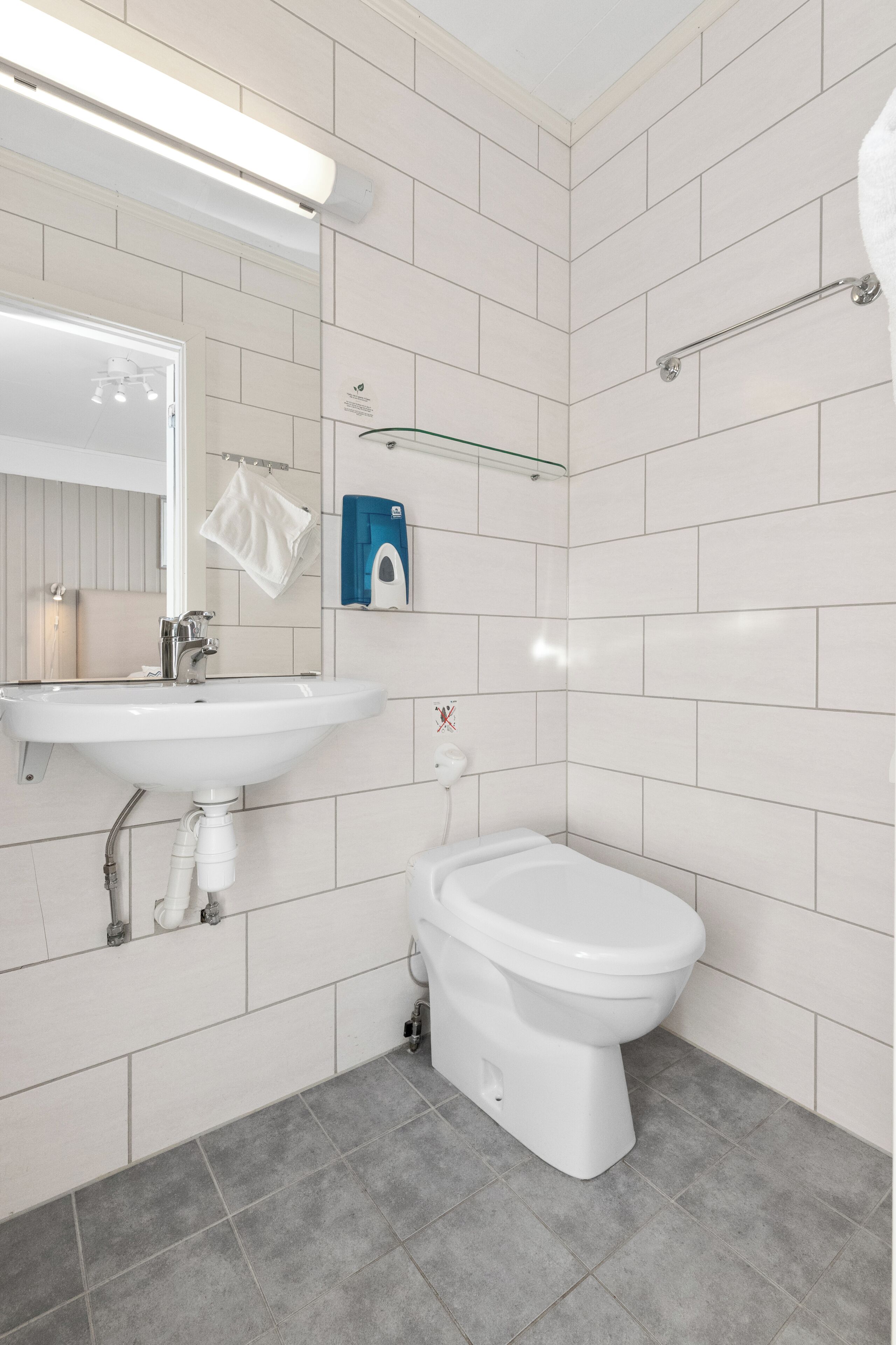 Une salle de bain avec un lavabo blanc, des toilettes et une étagère en verre.
