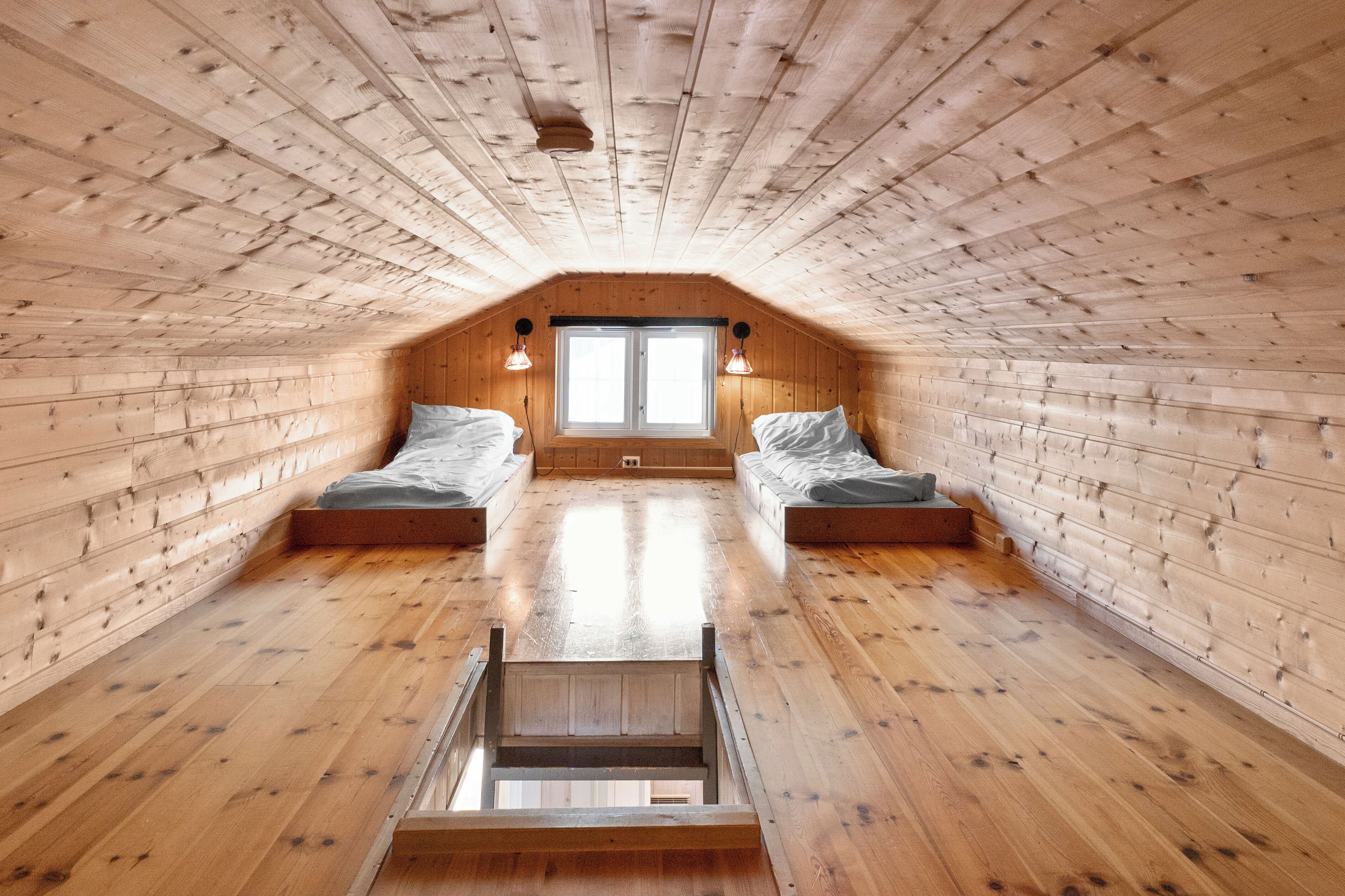 A wooden attic bedroom with two beds, a skylight, and a wooden staircase.