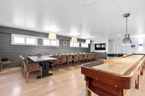 Une table de billard, une longue table à manger avec des chaises et un téléviseur dans une pièce moderne dotée de planchers en bois et de murs blancs.