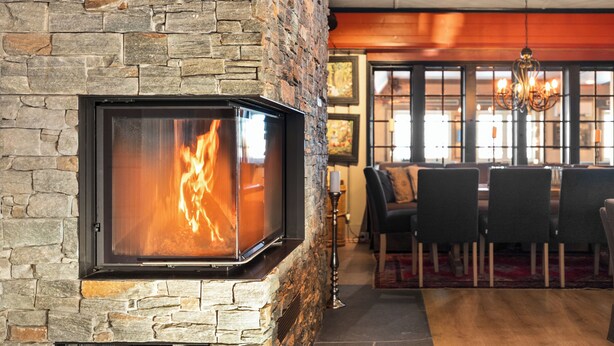 A stone fireplace with a glass door, a dining area with chairs and a table, and a chandelier. - Gomobu Fjellstue (Vestre Slidre)