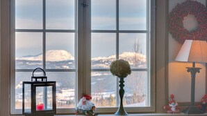 A cozy room with a large window, a decorative wreath, a lamp, and a small gnome figurine. - Gomobu Fjellstue (Vestre Slidre)