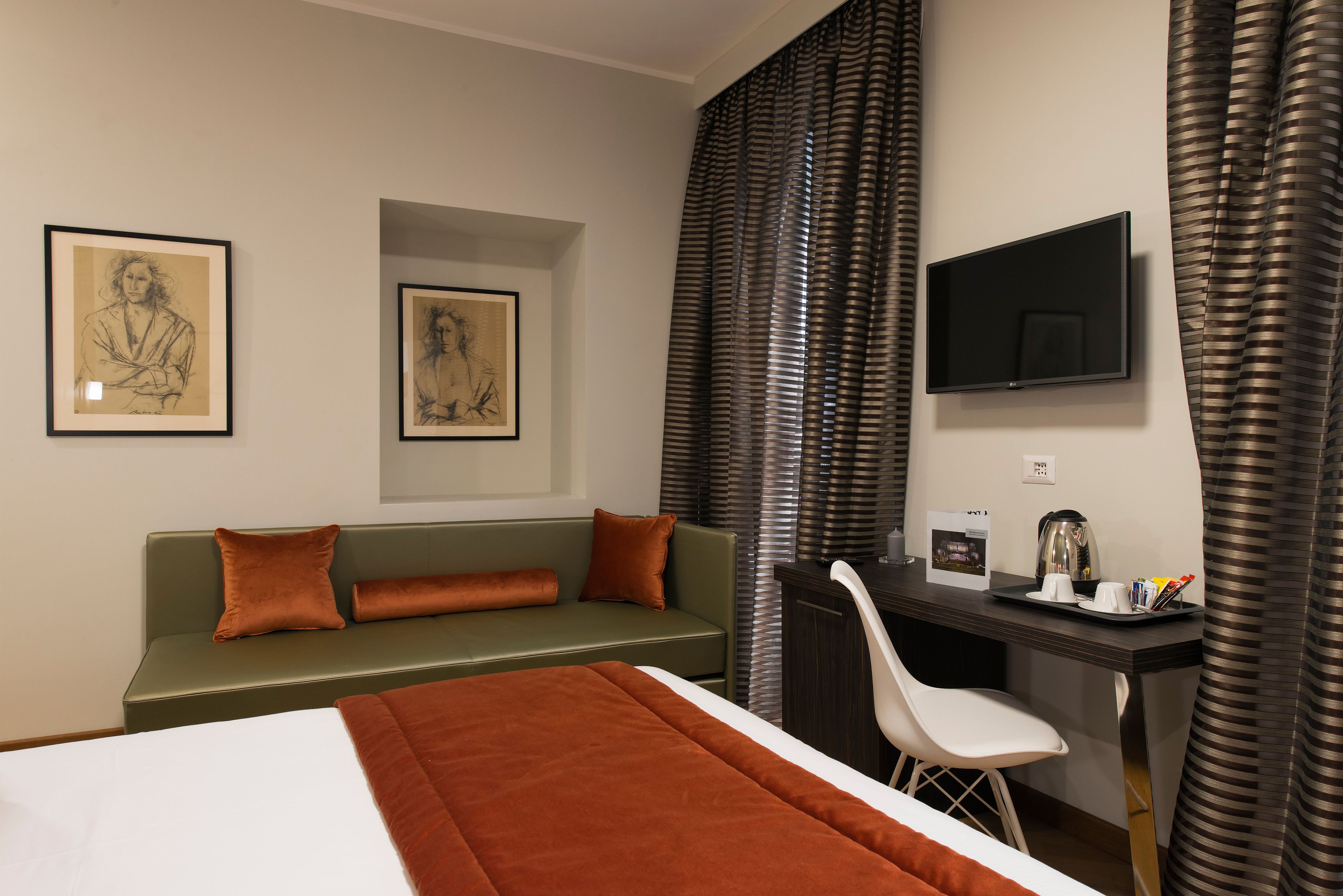 A hotel room with a bed, a desk, a chair, a TV, and two framed artworks on the wall.