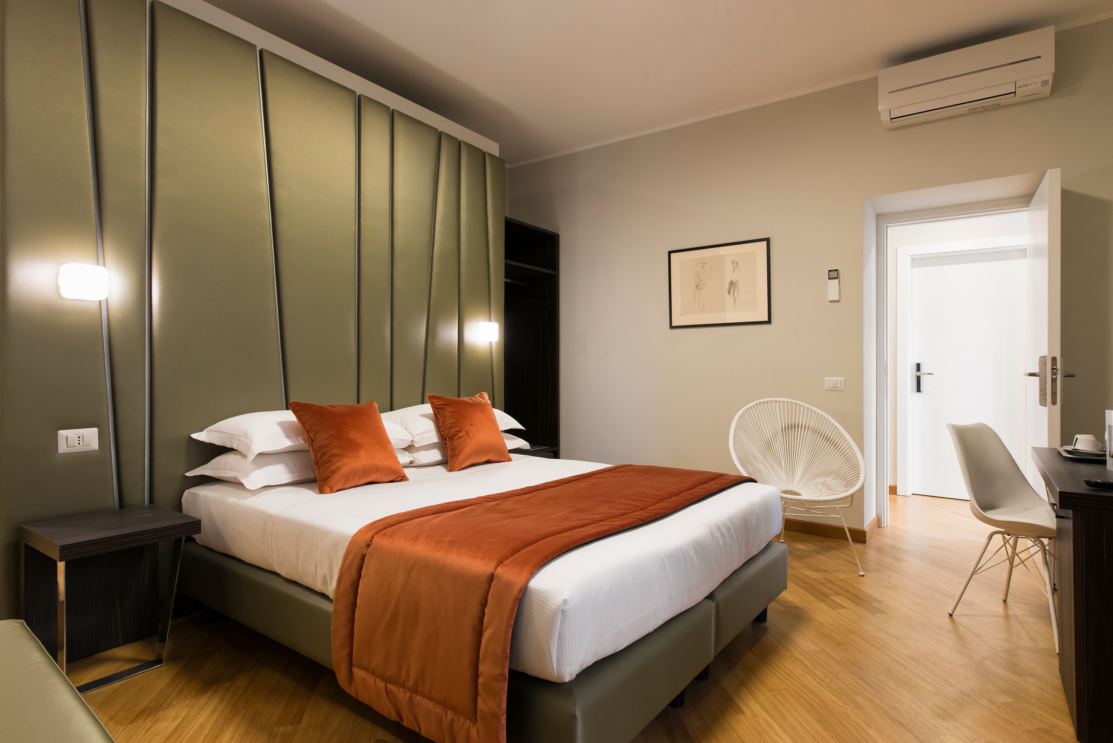 Habitació d'hotel moderna amb un llit gran, una taula de nit, una cadira i un escriptori.