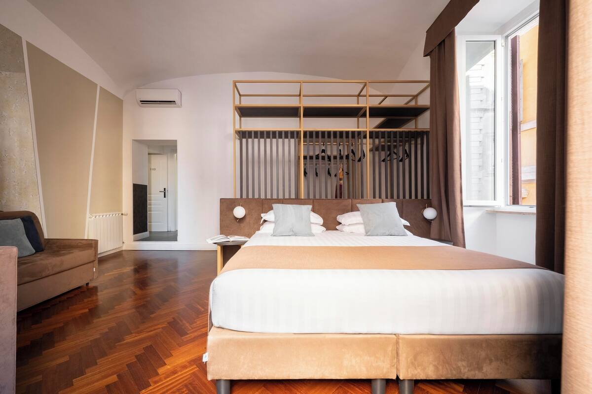 Habitación de hotel moderna con una cama grande, un cabecero de madera, un armario con espejo y vistas a la ciudad.
