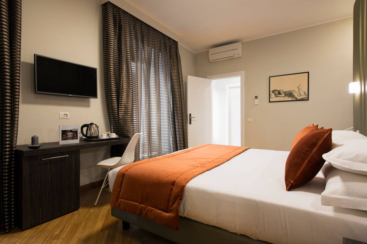 Una habitación de hotel con una cama, un escritorio, una silla, un televisor y una ventana con cortinas.