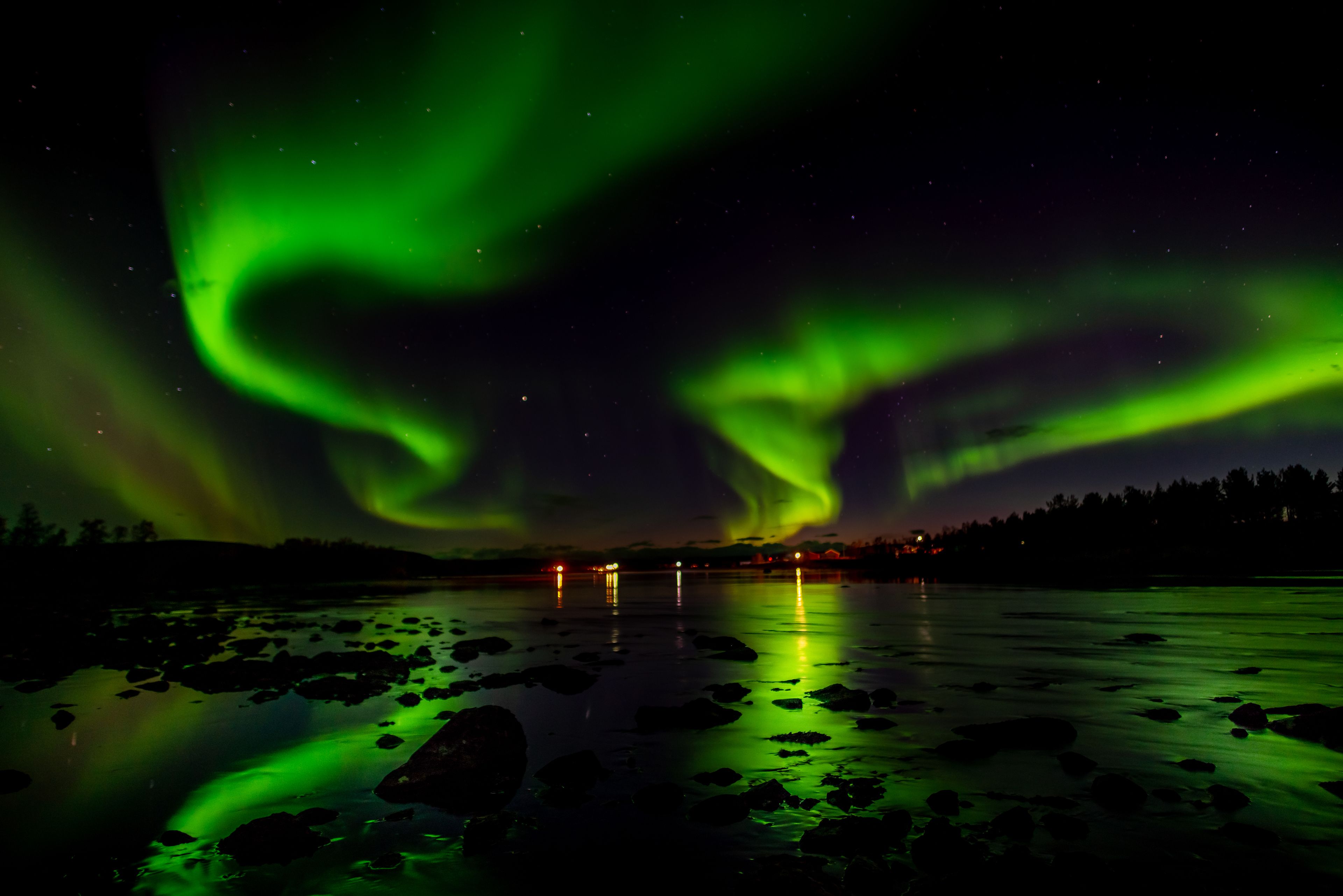 Una vista nocturna de las auroras boreales sobre un río tranquilo con rocas, iluminado por una aurora verde.