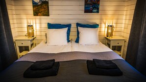 A neatly made bed with two pillows, a headboard, and two bedside tables with lamps. - Arctic gourmet cabin (Kiruna)