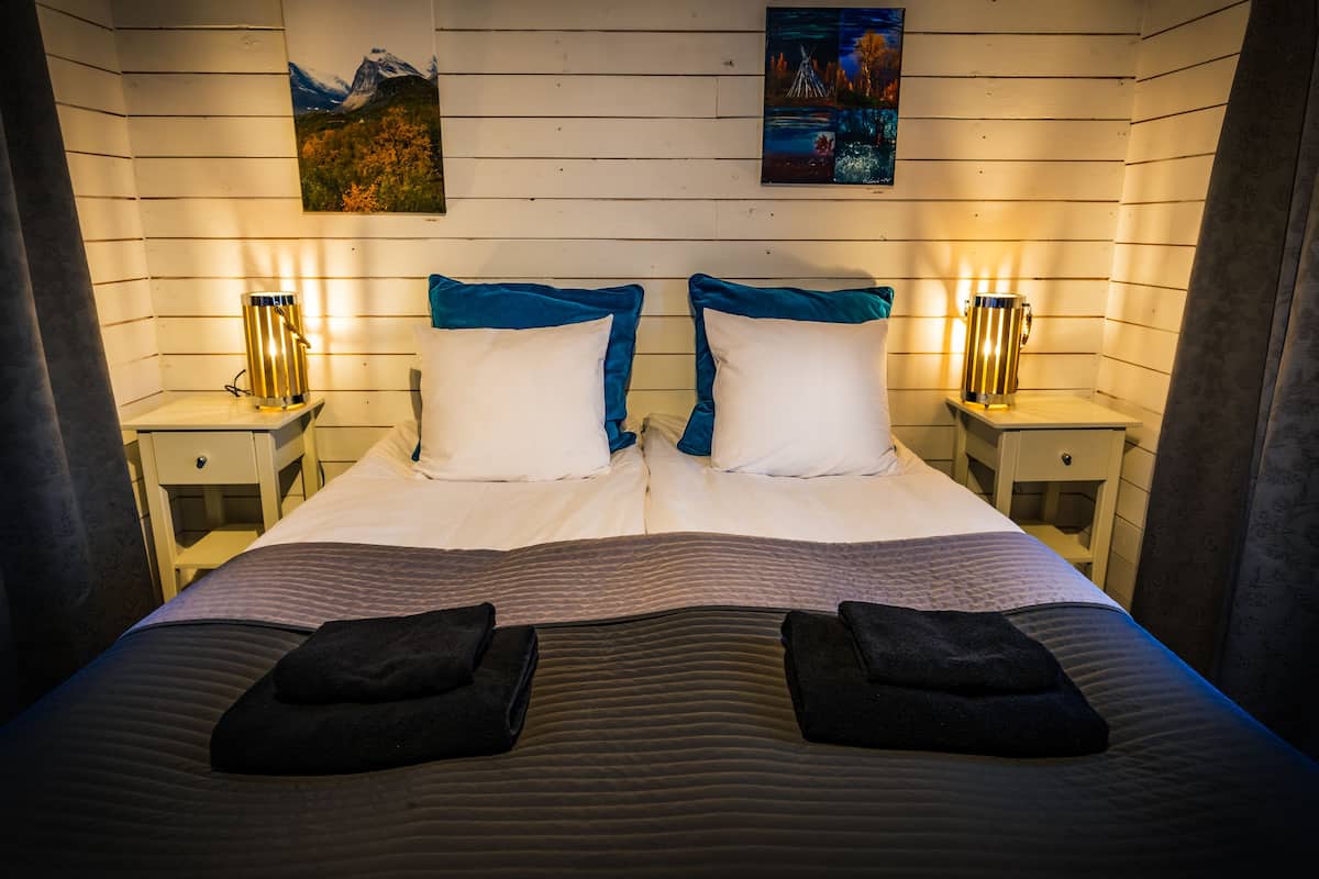 A neatly made bed with two pillows, a headboard, and two bedside tables with lamps.