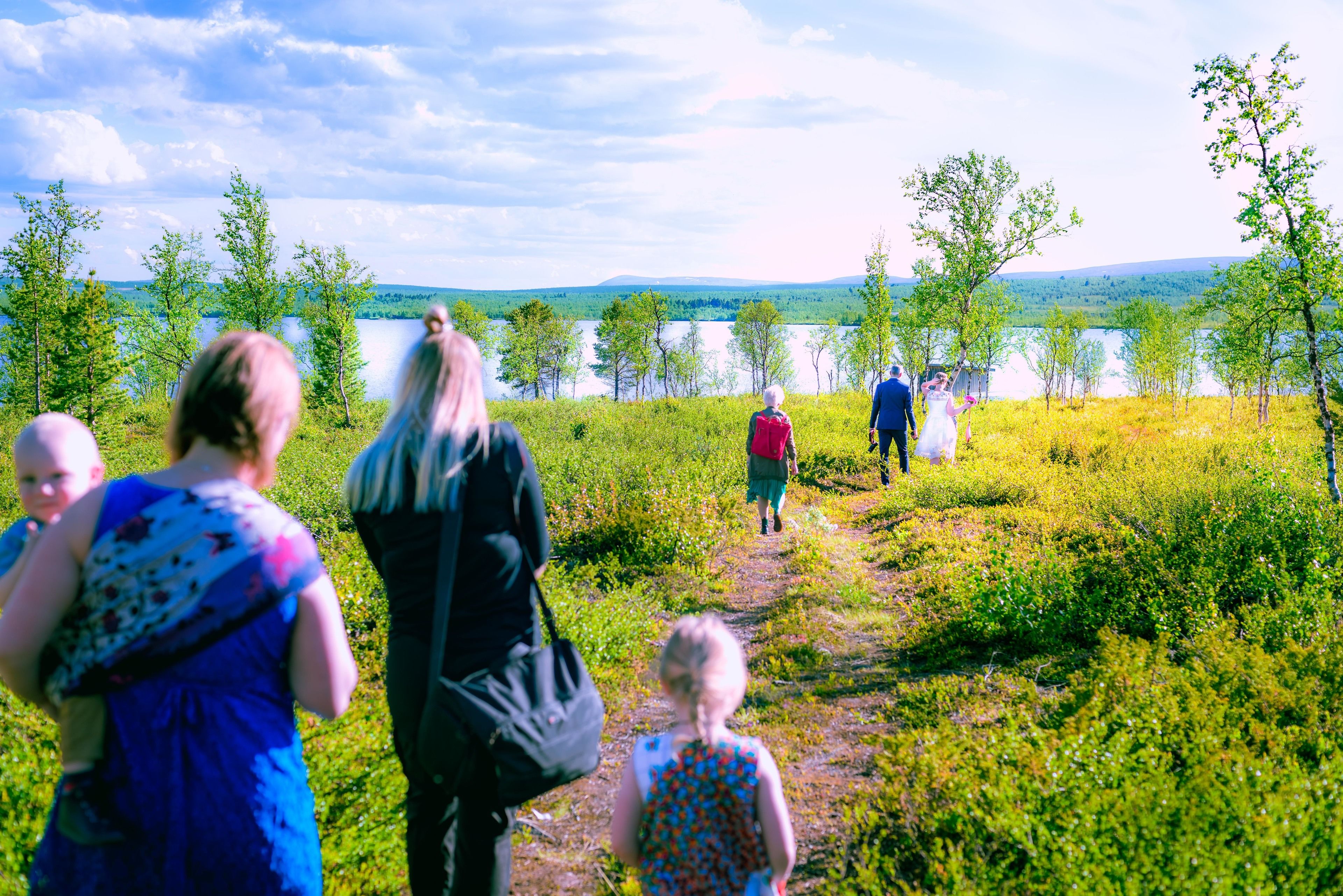 Un grupo de personas caminando por un sendero junto a un lago, con árboles y colinas al fondo.
