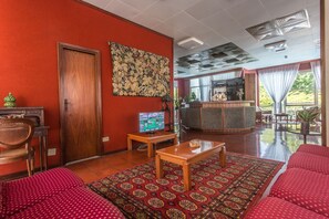 A hotel room with a red carpet, wooden furniture, a television, a wooden door, and a large window with curtains.