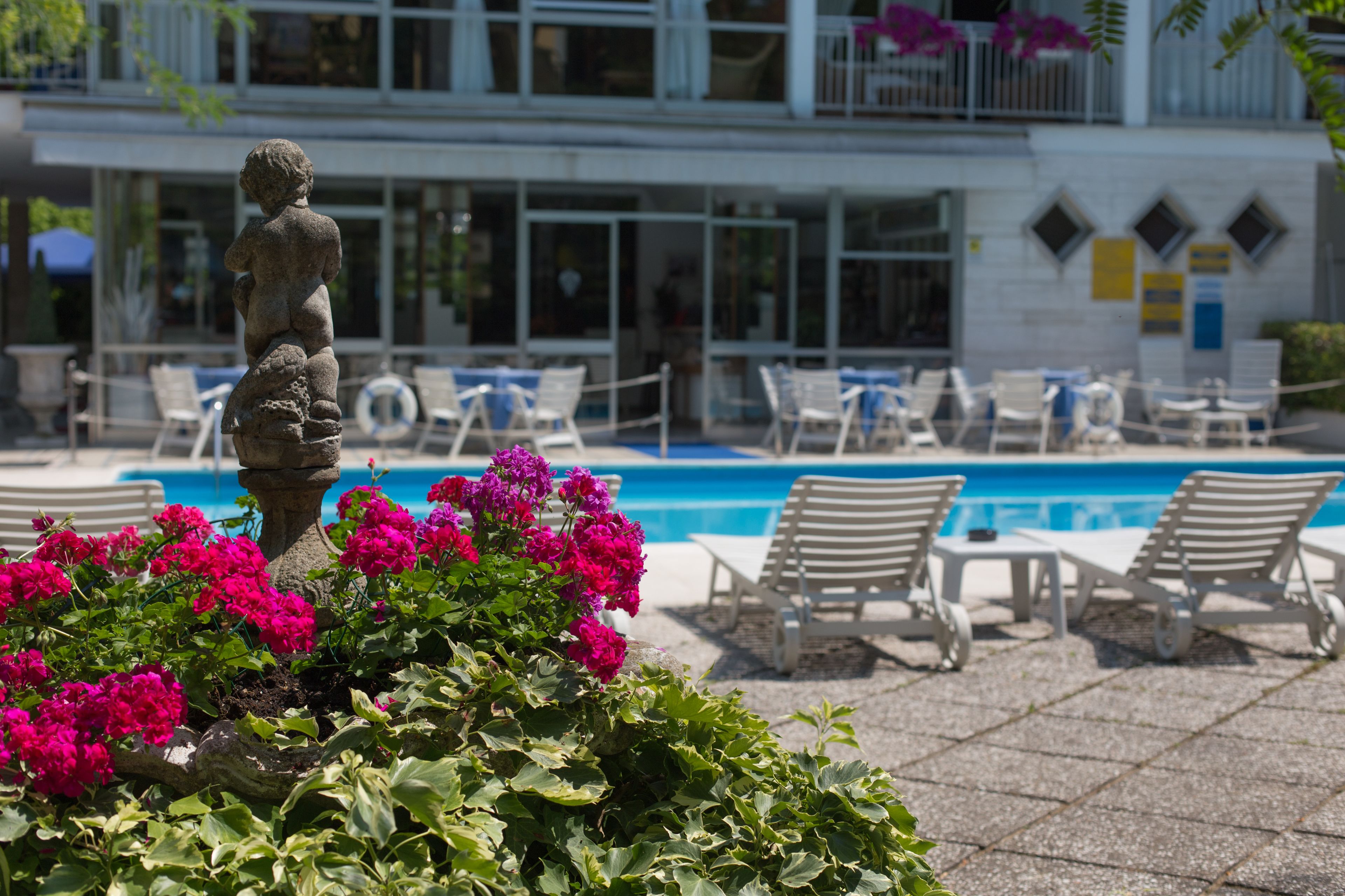 Area piscina con lettini, una statua e fiori colorati.