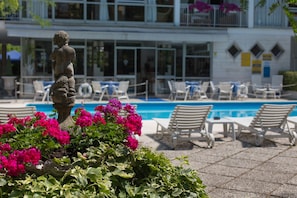 A poolside area with lounge chairs, a statue, and vibrant flowers.