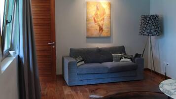 A living room with a grey sofa, a wooden floor, a painting on the wall, and a floor lamp.