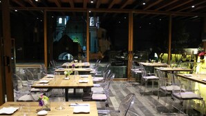 A restaurant with clear glass tables and chairs, a wooden ceiling, and a view of a building in the background. - Hotel Casa Mixtli (Teziutlan)