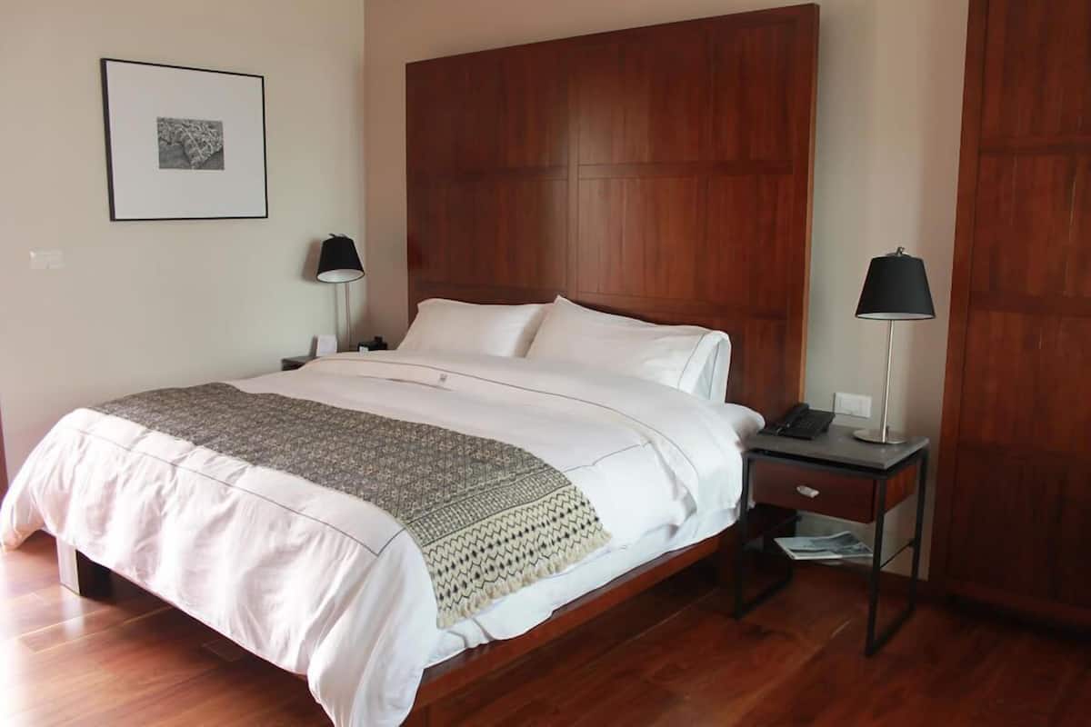 A neatly made bed with a patterned throw, a wooden headboard, two bedside tables with lamps, and a framed picture on the wall.