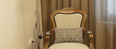 Una habitación con piso de madera, un sillón estampado con un cojín, una lámpara de pie y un cuadro en la pared.